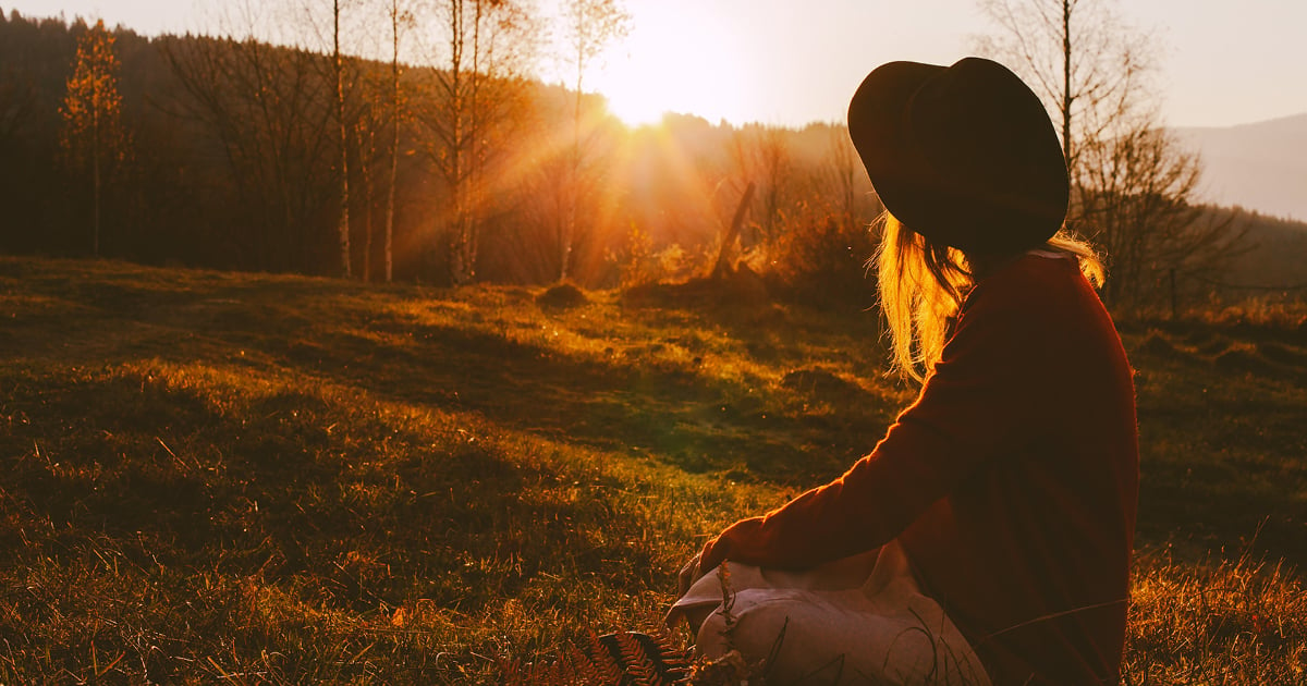 Today's daily devotional -  A woman watching the sunset over the woods.